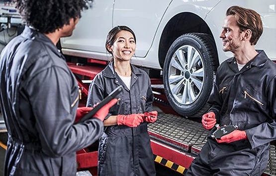three people in workshop infront of a car